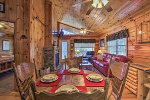 A wooden cabin interior with a dining table set for four, a leather sofa, and a fireplace.