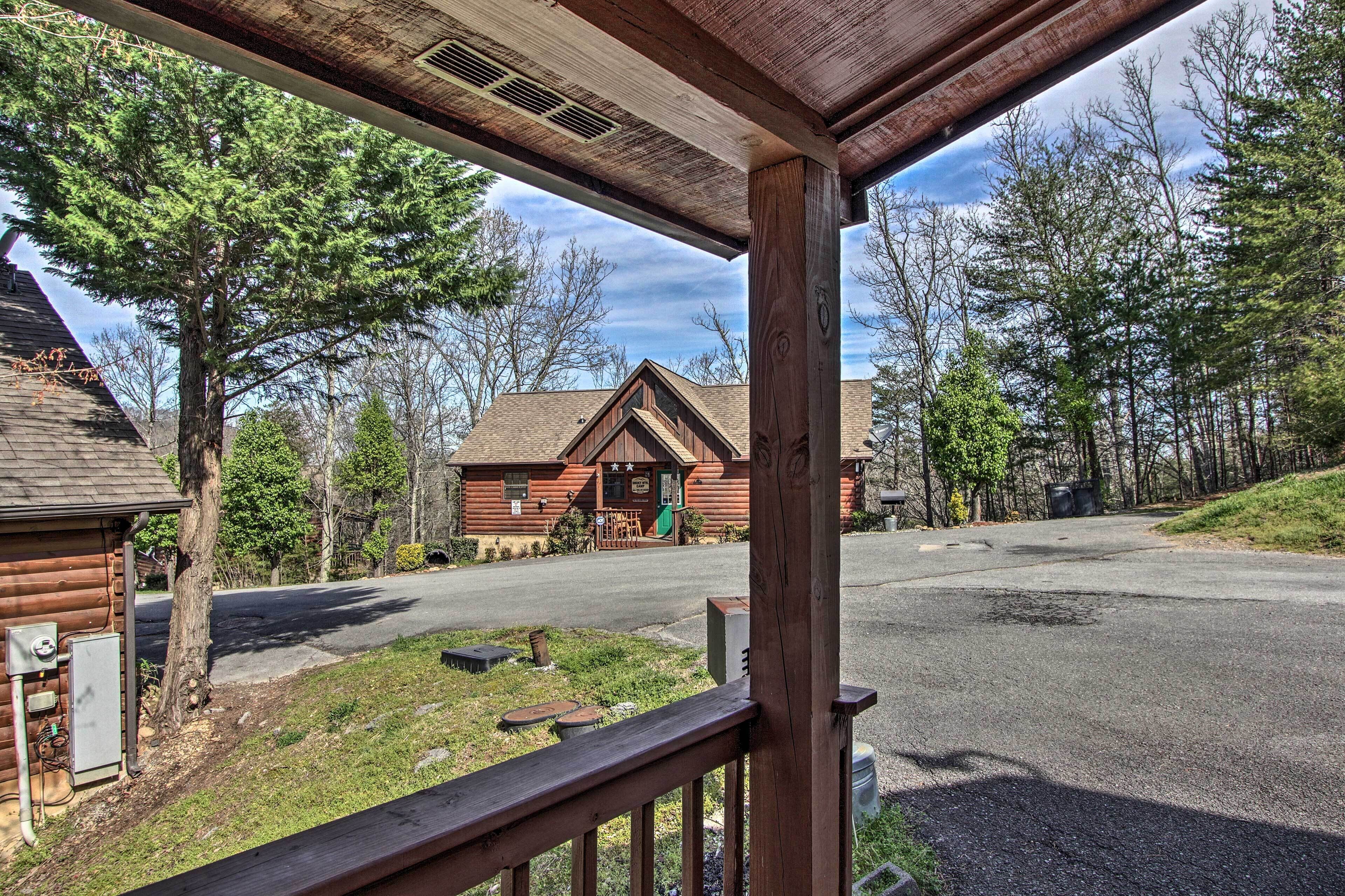 Une cabane en bois avec une véranda, une route devant et des arbres tout autour.