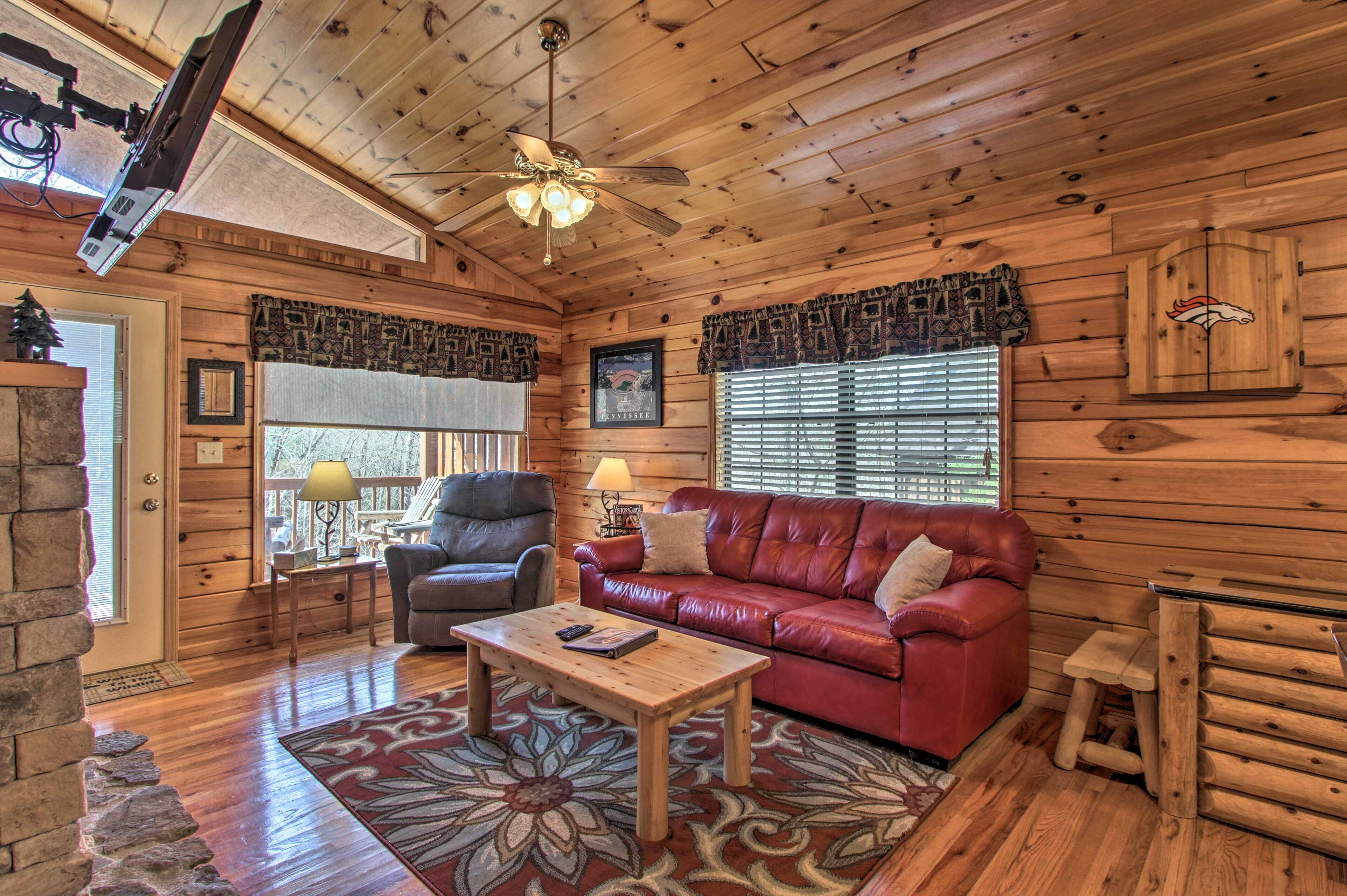 A log cabin interior with a wooden ceiling, a red leather sofa, a wooden coffee table, and a ceiling fan.