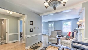 A spacious living room with a leather sofa, a chair, and a wooden coffee table. There is a chandelier and a fireplace with a lamp. - Historic Townhome in Downtown Shepherdstown! (Shepherdstown)