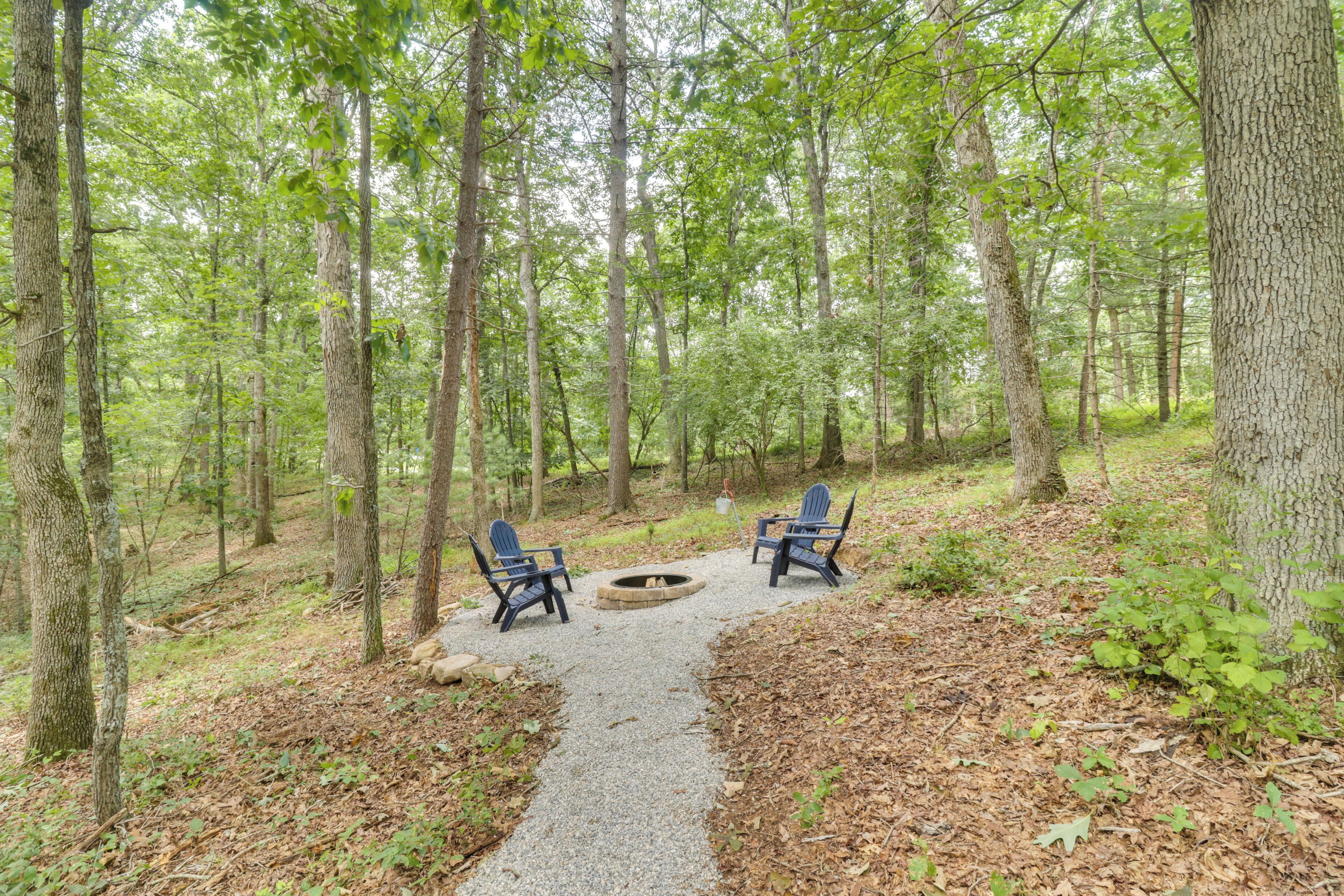Um camping arborizado com duas cadeiras Adirondack e um poço de fogo.