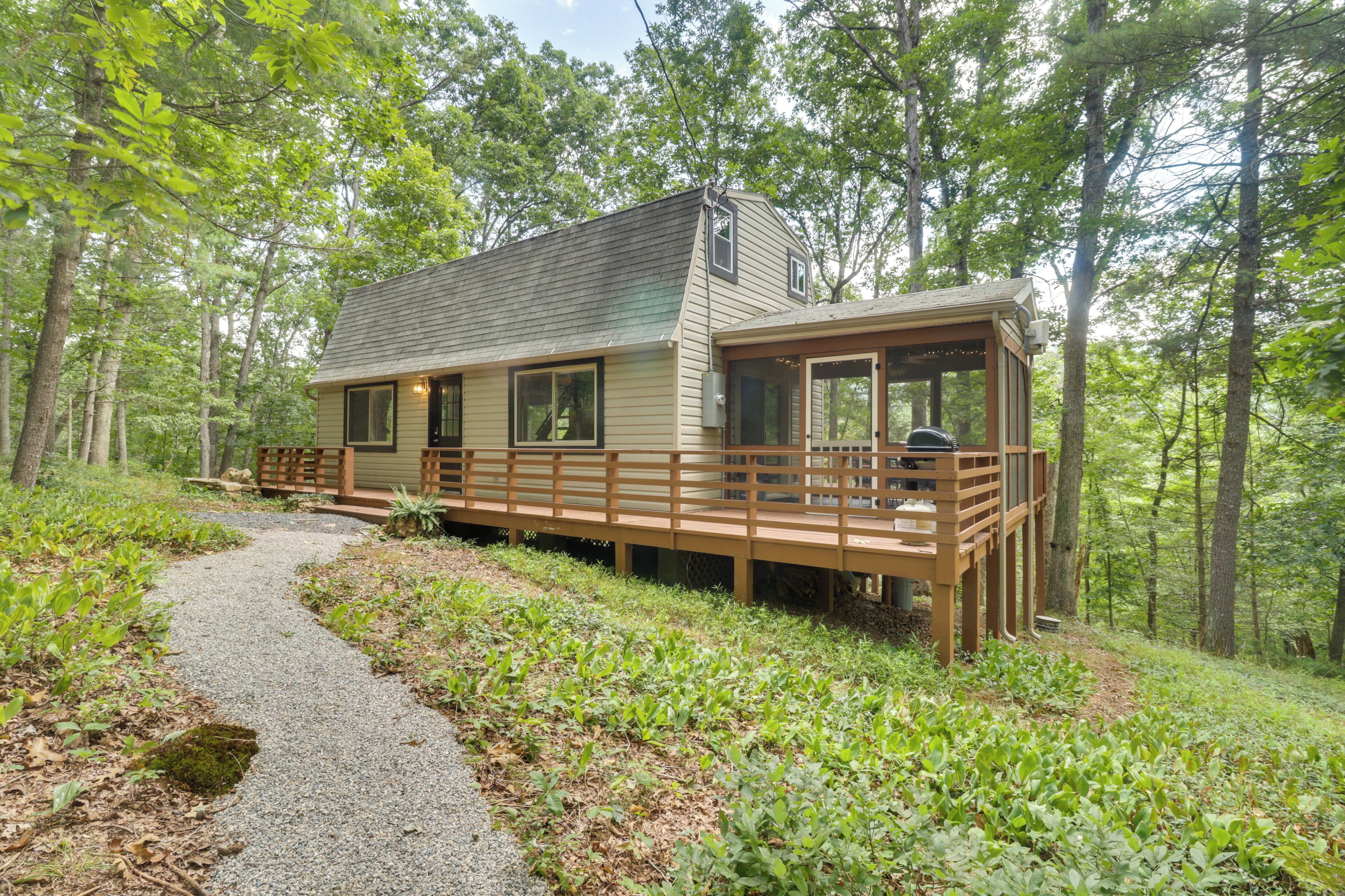 A cabin with a deck, surrounded by a forest.