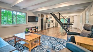 A spacious living room with a large window, a staircase leading to a kitchen, and a cozy seating area. - Private Hot Tub & Fire Pit: Family Broadway Cabin (Broadway)