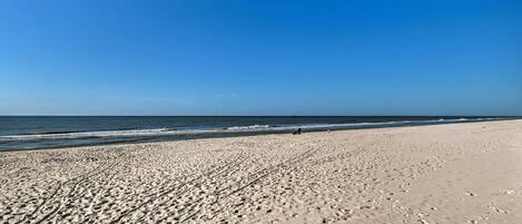 A wide sandy beach with gentle waves and a clear blue sky.