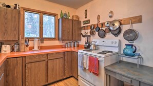 A kitchen with wooden cabinets, a white stove, and various pots and pans hanging on the wall. - Idyllic Northport Cottage, Walk to Lakeside! (Northport)
