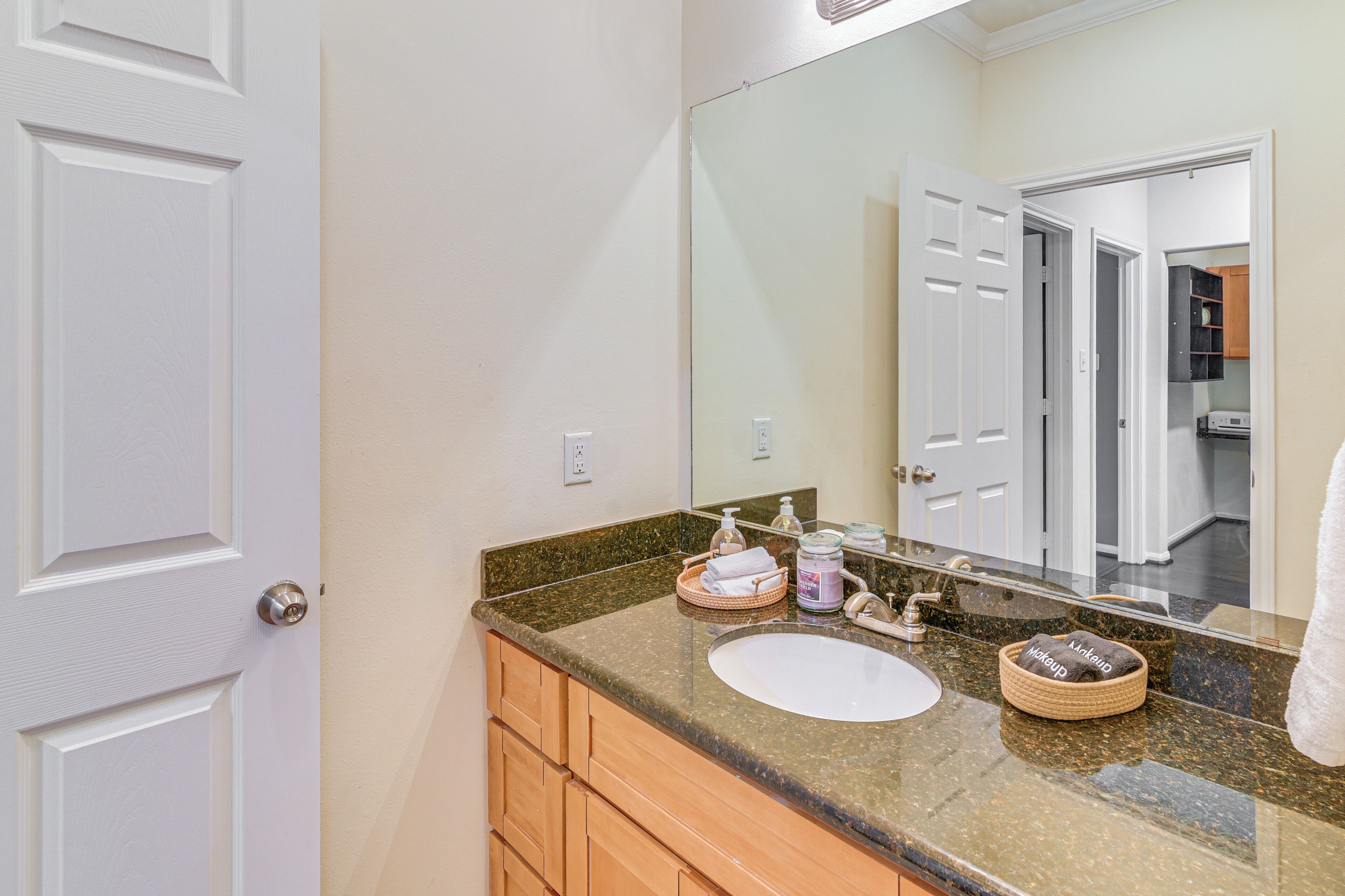 A bathroom with a white sink, a large mirror, wooden cabinets, and a granite countertop.