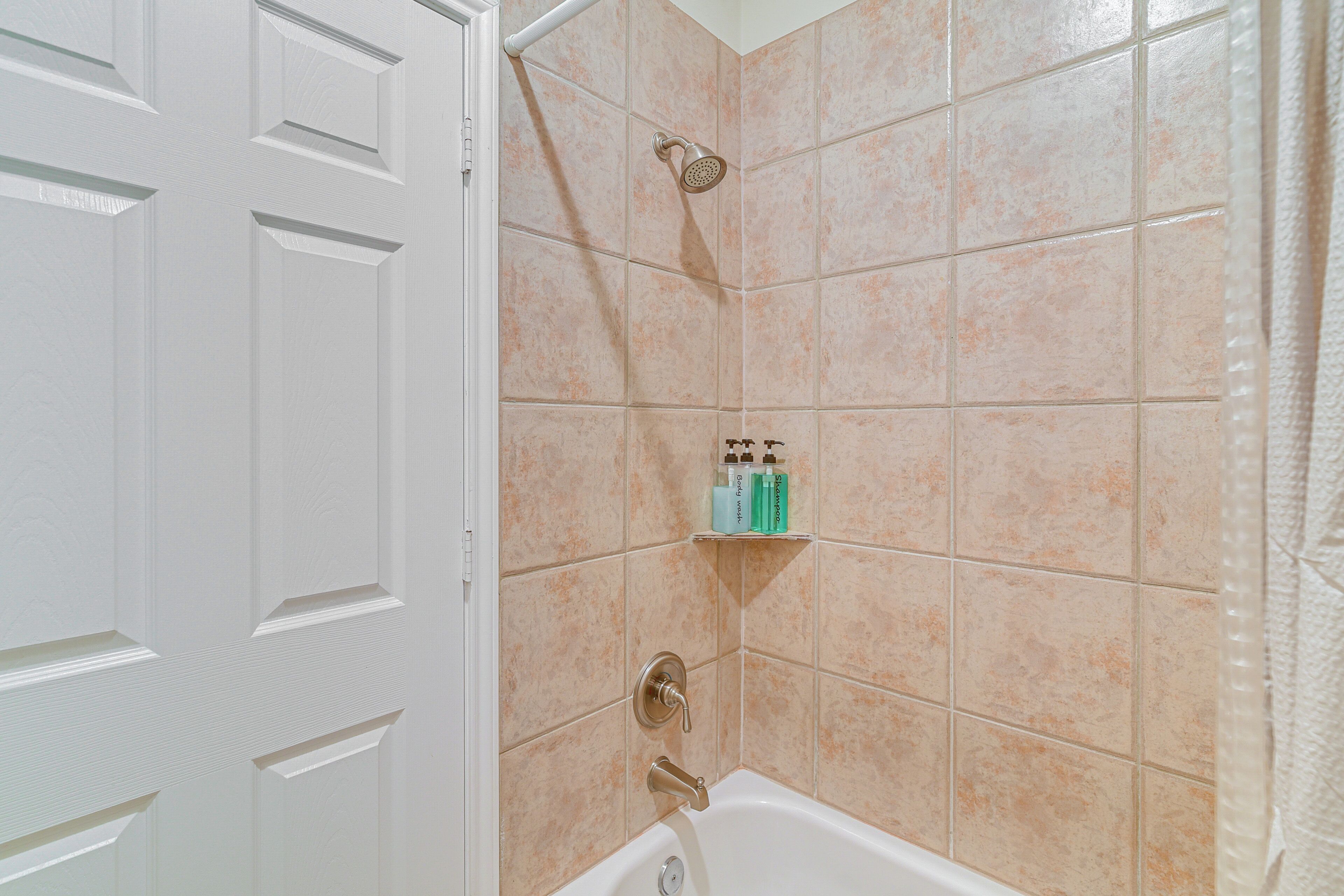 A bathroom with beige tiles, a shower, and a shelf with toiletries.