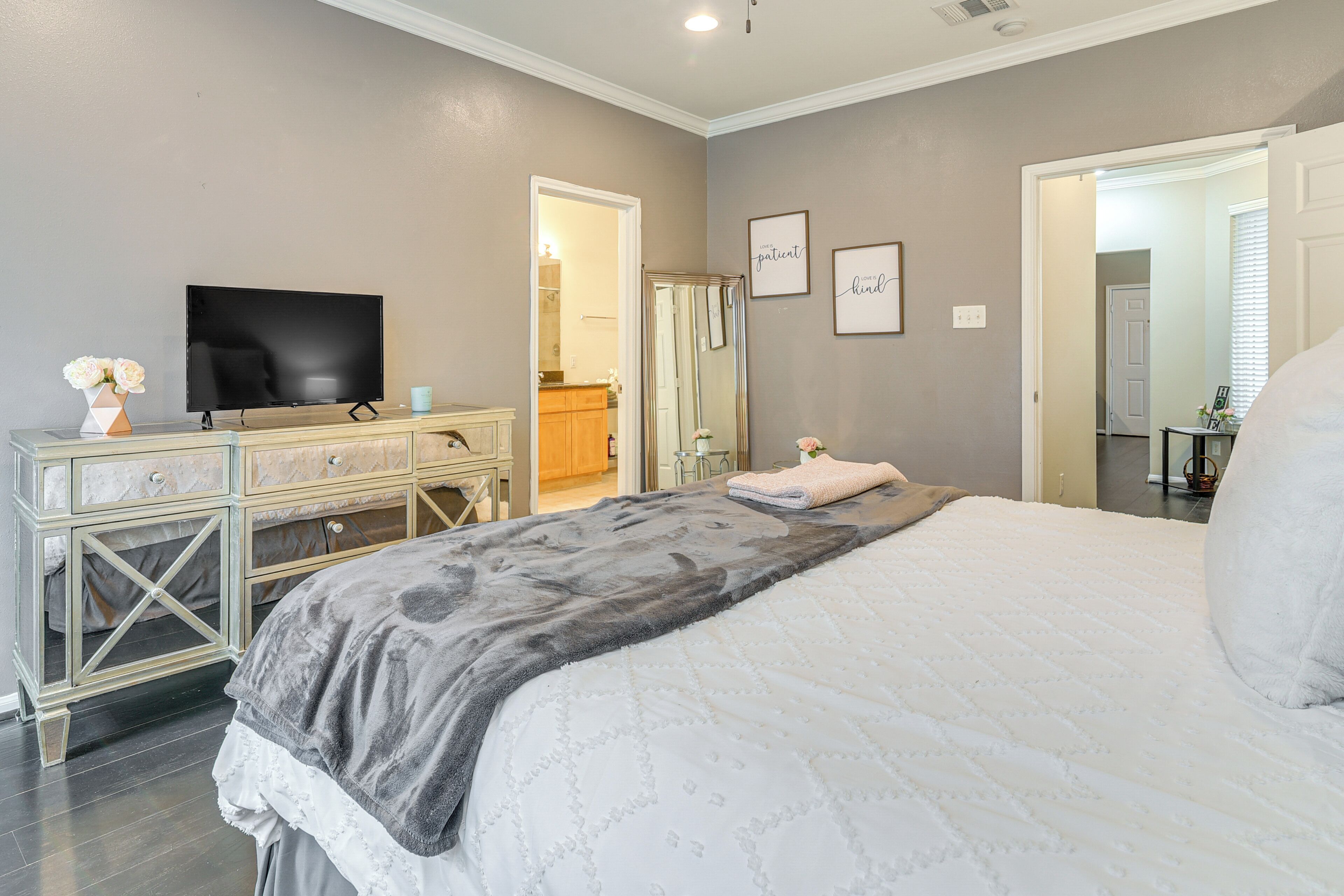 Een slaapkamer met een bed, een dressoir, een televisie en een badkamer die door een geopende deur zichtbaar is.