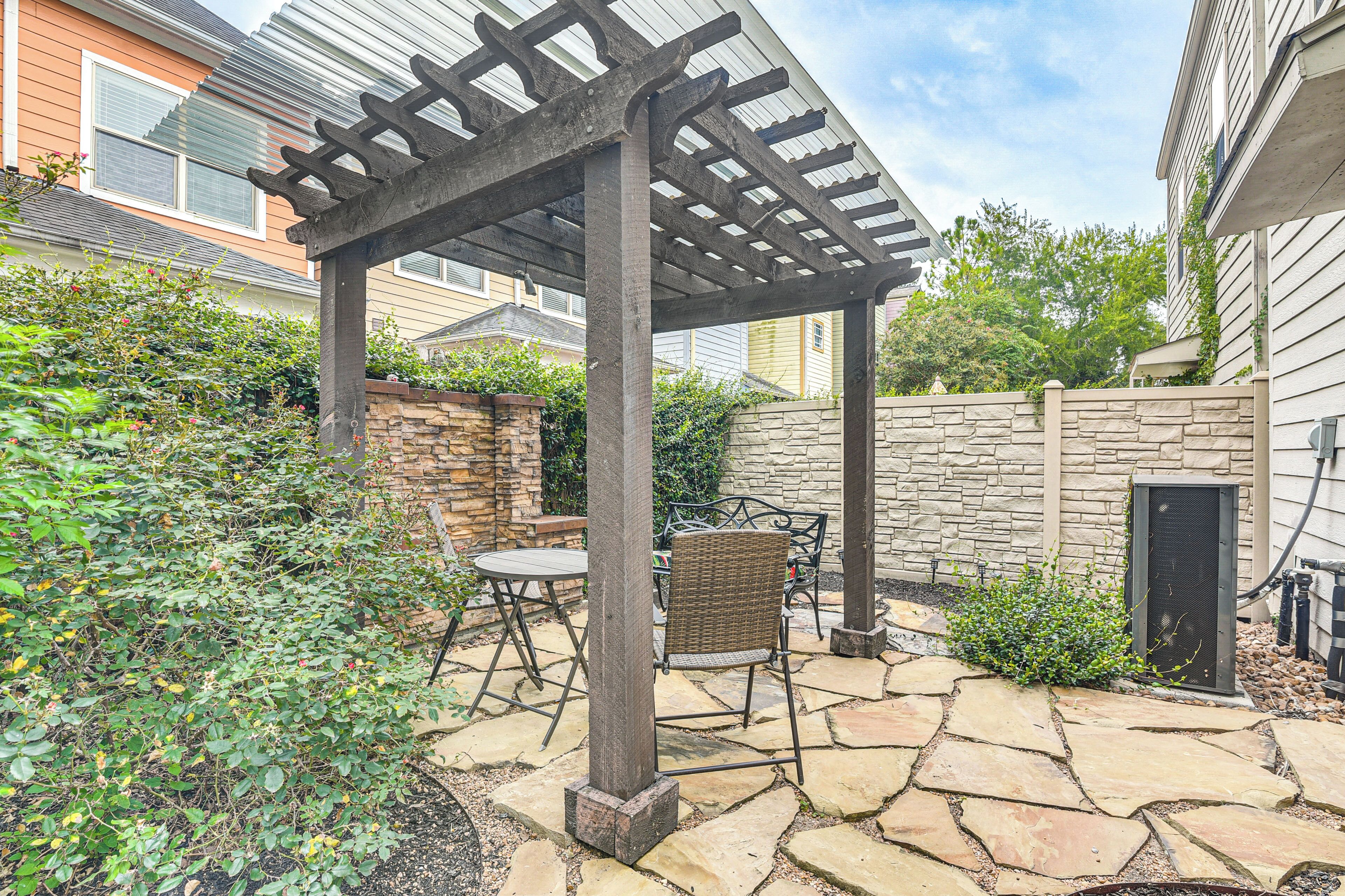 Un patio cubierto con suelo de piedra, una pérgola y mobiliario exterior.