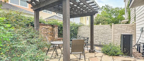 Un patio cubierto con suelo de piedra, una pérgola y mobiliario exterior.
