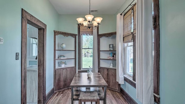 A dining area with a wooden table and chairs, a chandelier, and wooden shelving with decorative items. - Lake Charles Cottage w/ Fireplace & Yard! (Lake Charles)