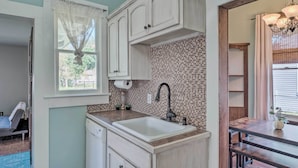 A kitchen with white cabinets, a tiled backsplash, a sink, and a wooden dining table. - Lake Charles Cottage w/ Fireplace & Yard! (Lake Charles)