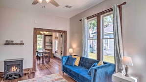 A cozy living room with a blue sofa, a fireplace, and a dining area visible through an open door. - Lake Charles Cottage w/ Fireplace & Yard! (Lake Charles)