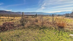 A rural landscape with a wooden fence and a metal gate, surrounded by grassy fields and distant mountains under a clear sky. - Home w/ Hot Tub Near Shenandoah Nat'l Park! (Bentonville)