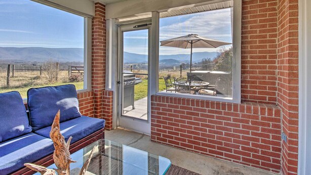 A covered patio with a glass table, blue cushioned seating, and a view of a barbecue area. - Home w/ Hot Tub Near Shenandoah Nat'l Park! (Bentonville)