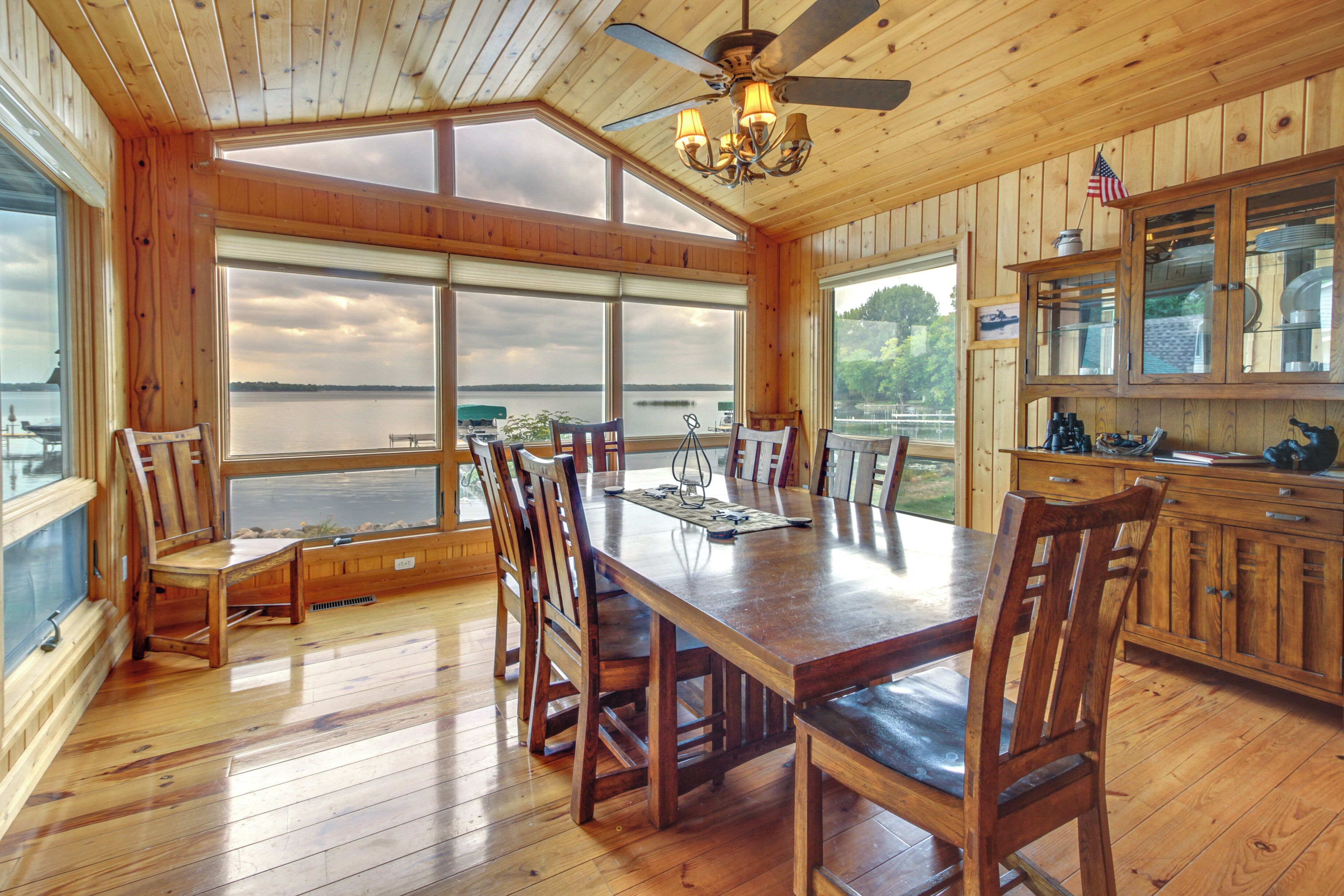 A wooden dining room with a large table and chairs, a ceiling fan, and a view of a lake.