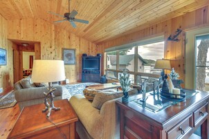 Un interior de cabaña acogedor con paredes de madera, un ventilador de techo, un sofá, una mesa de centro y un comedor con una mesa de vidrio y objetos decorativos.
