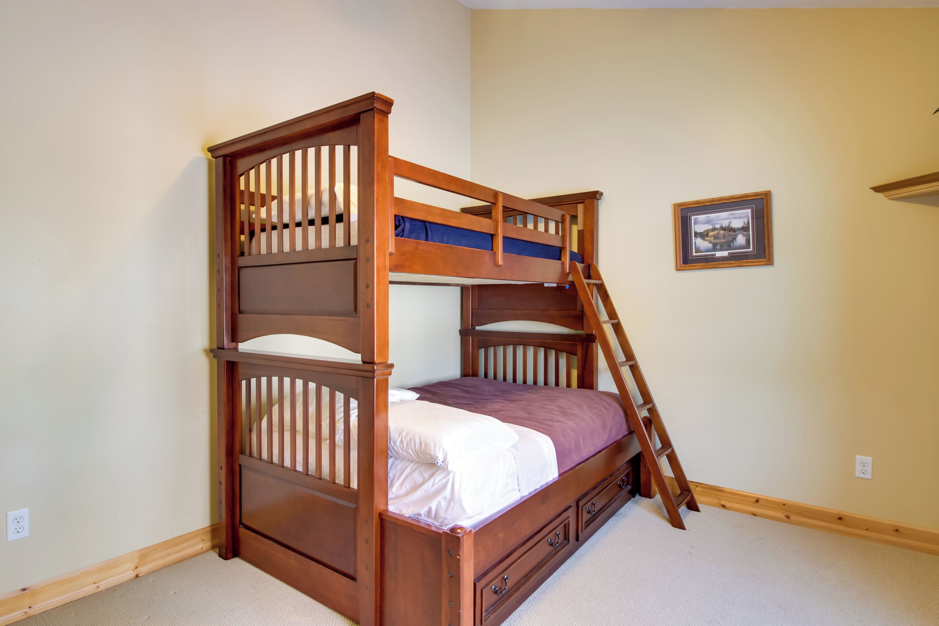 A bunk bed with a ladder, a small bedside table, and a framed picture on the wall.