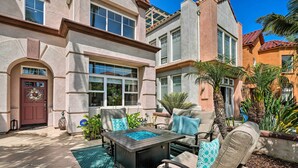 A patio area with a fire pit table, outdoor seating, and a view of a house with a large arched doorway and a wreath on the door. - Oceanside Home w/ Rooftop Patio, Walk to Beach! (Oceanside)