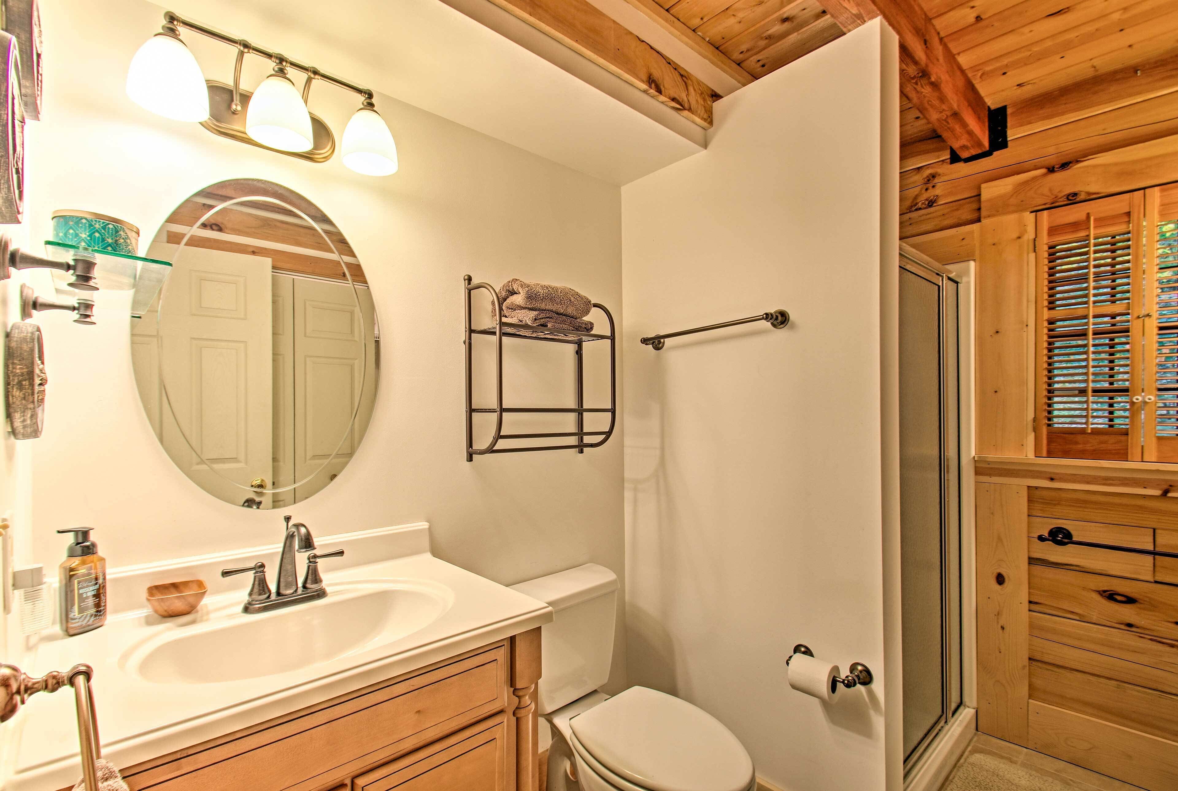A bathroom with a wooden ceiling, a white sink, a mirror, a towel rack, and a shower area.