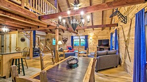 L’intérieur d’un chalet en bois comprend une table à manger, des chaises, un canapé, un téléviseur et un escalier.