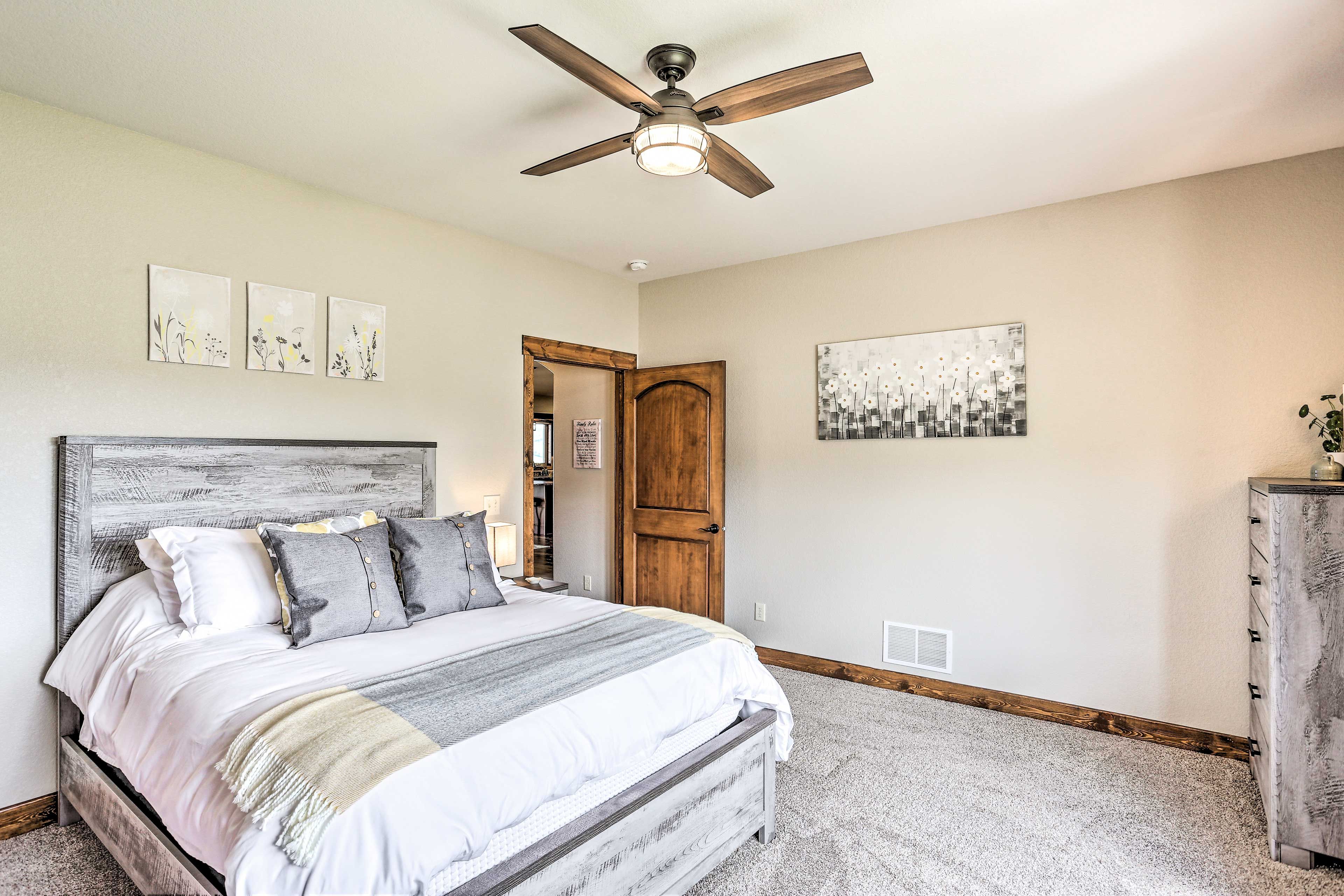 A bedroom with a bed, a ceiling fan, a wooden door, and a dresser.