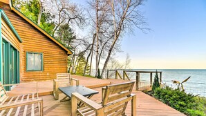 Una terraza de madera con mobiliario exterior, vista al agua y una cabaña de madera.