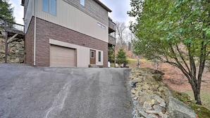 A two-story building with a garage, a stone retaining wall, and a tree in the foreground. - Steps to Beech Mountain Resort: Cozy Getaway (Banner Elk)