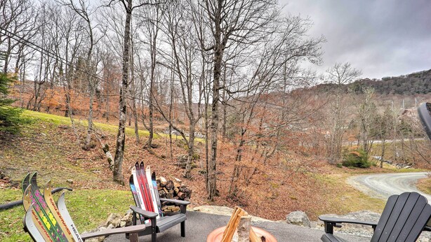 A deck with Adirondack chairs and a fire pit, overlooking a wooded area with a winding road. - Steps to Beech Mountain Resort: Cozy Getaway (Banner Elk)