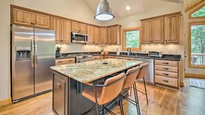 A modern kitchen with a central island, stainless steel appliances, wooden cabinets, and a large window providing natural light. - Luxe Wintergreen Resort Escape w/ Hot Tub! (Nellysford)
