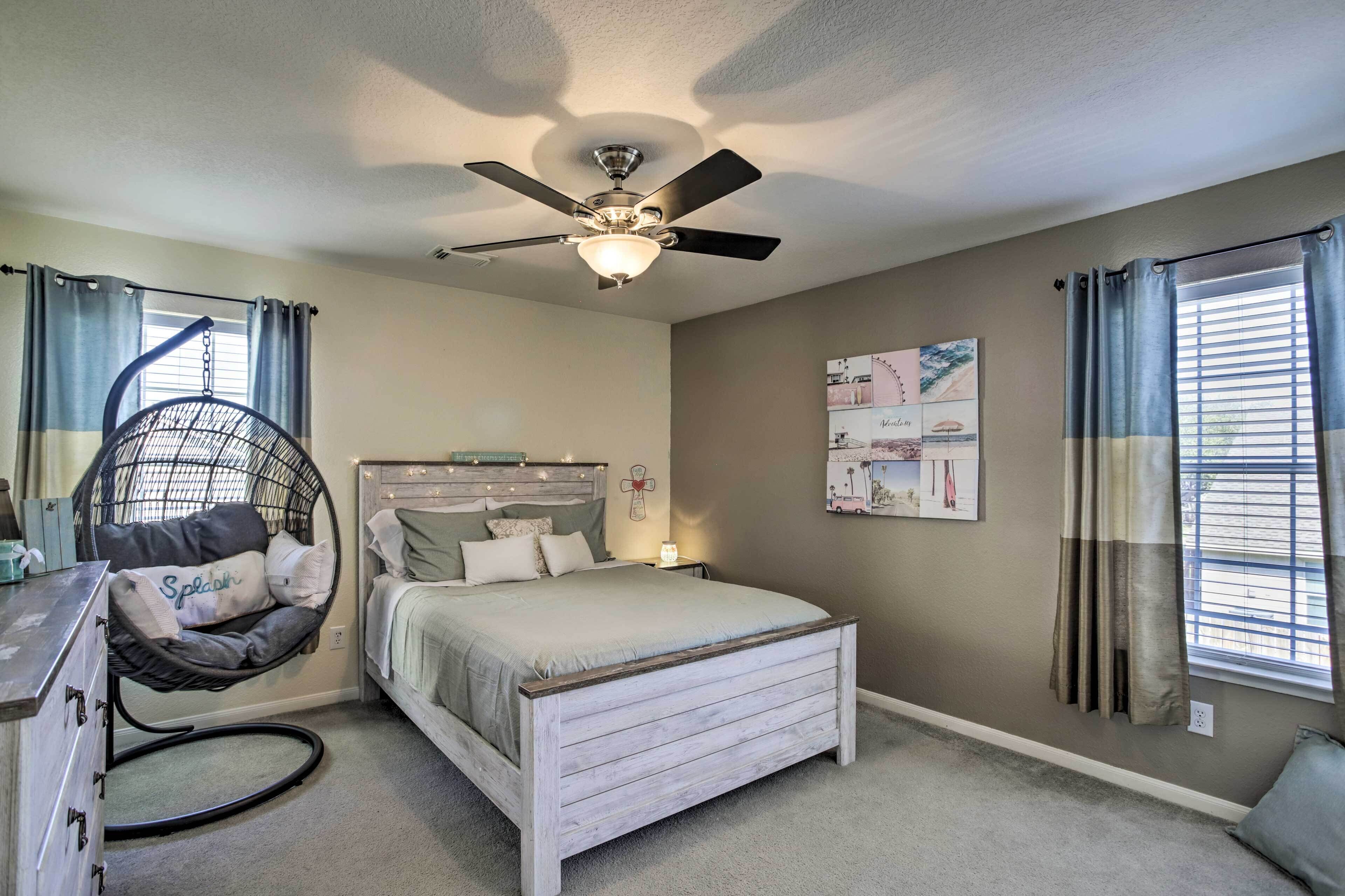 A bedroom with a bed, a hanging chair, a ceiling fan, and a window with curtains.