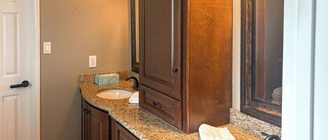 A bathroom with a granite countertop, two sinks, a mirror, and wooden cabinetry.