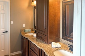 A bathroom with a granite countertop, two sinks, a mirror, and wooden cabinetry. - Luxe Home 30 Miles to Houston w/ Pool & Grill (Cypress)