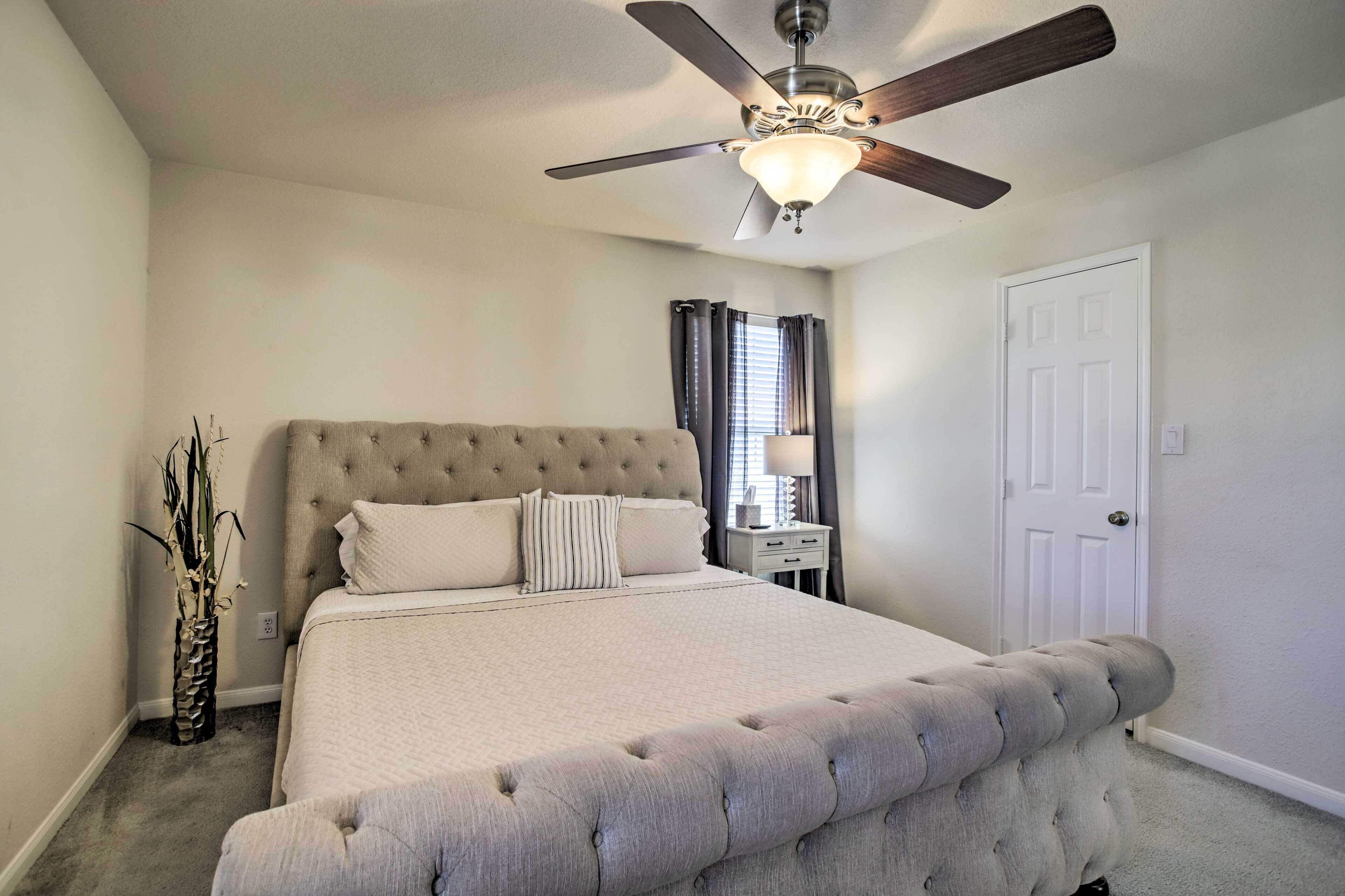 A bedroom with a large bed, a ceiling fan, a nightstand, and a door.