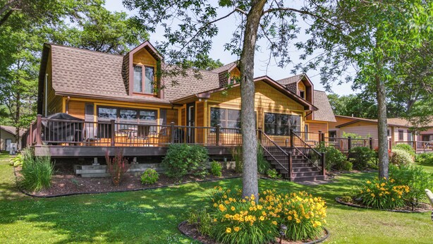 A two-story wooden house with a balcony, surrounded by a well-maintained garden with yellow flowers. - Large Home on Lake Edward w/ Deck & Fire Pit! (Nisswa)