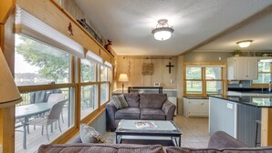 A cozy living room with a sofa, a coffee table, and a dining area with a table and chairs. There is a kitchen area with cabinets and a countertop. - Large Home on Lake Edward w/ Deck & Fire Pit! (Nisswa)