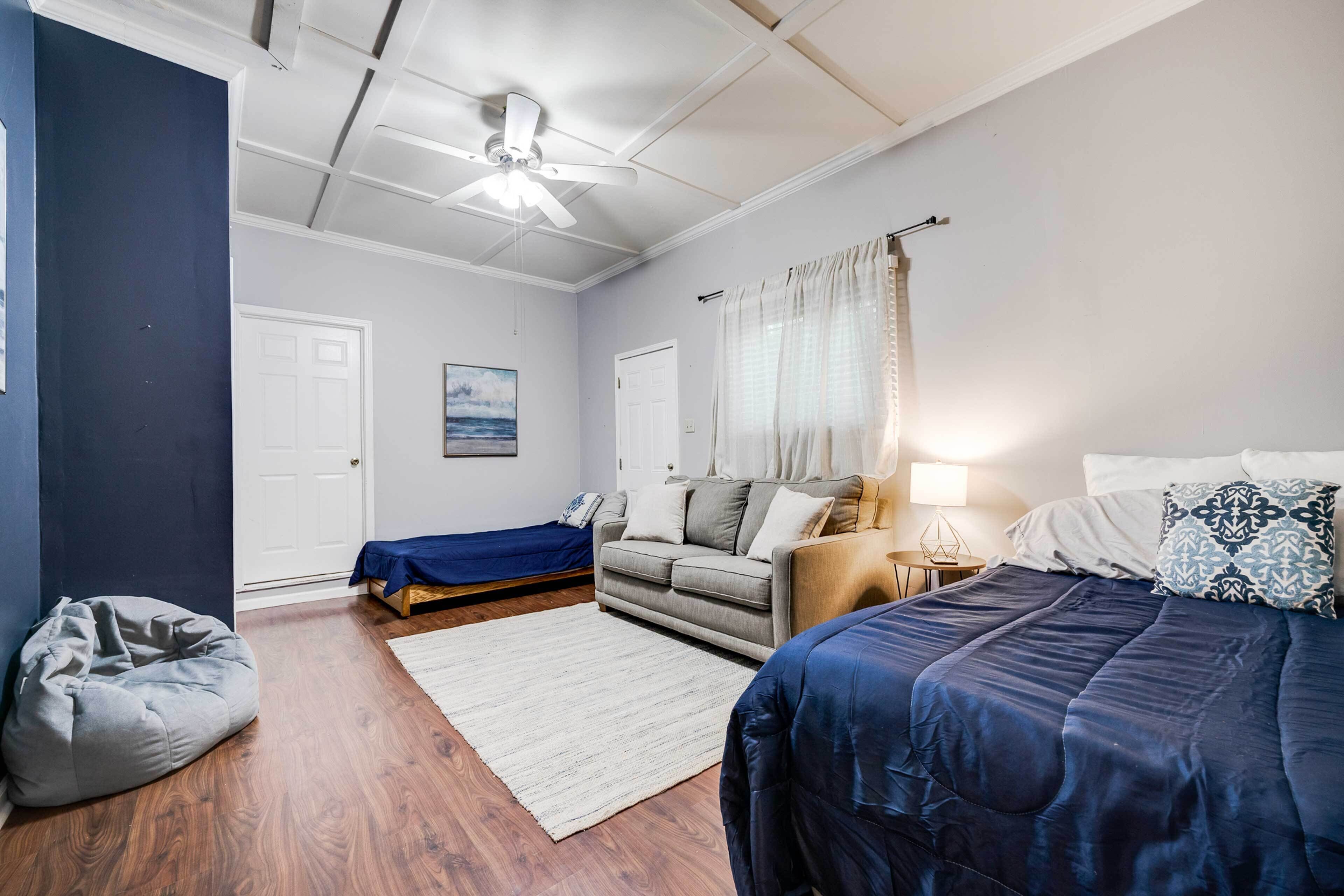 A bedroom with a bed, a sofa, a chair, a desk, and a ceiling fan.