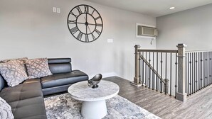 A modern living room with a black leather sofa, a marble coffee table, and a large wall clock. - Modern Indianapolis Home w/ Skyline Views (Indianapolis)