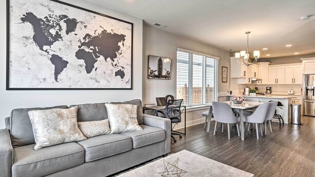 A modern living room with a gray sofa, a coffee table, and a dining area with chairs and a table. - Modern Indianapolis Home w/ Skyline Views (Indianapolis)