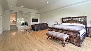 Un dormitorio amplio con una cama grande, un cabecero de madera oscura, un banco de madera y un televisor en la pared.