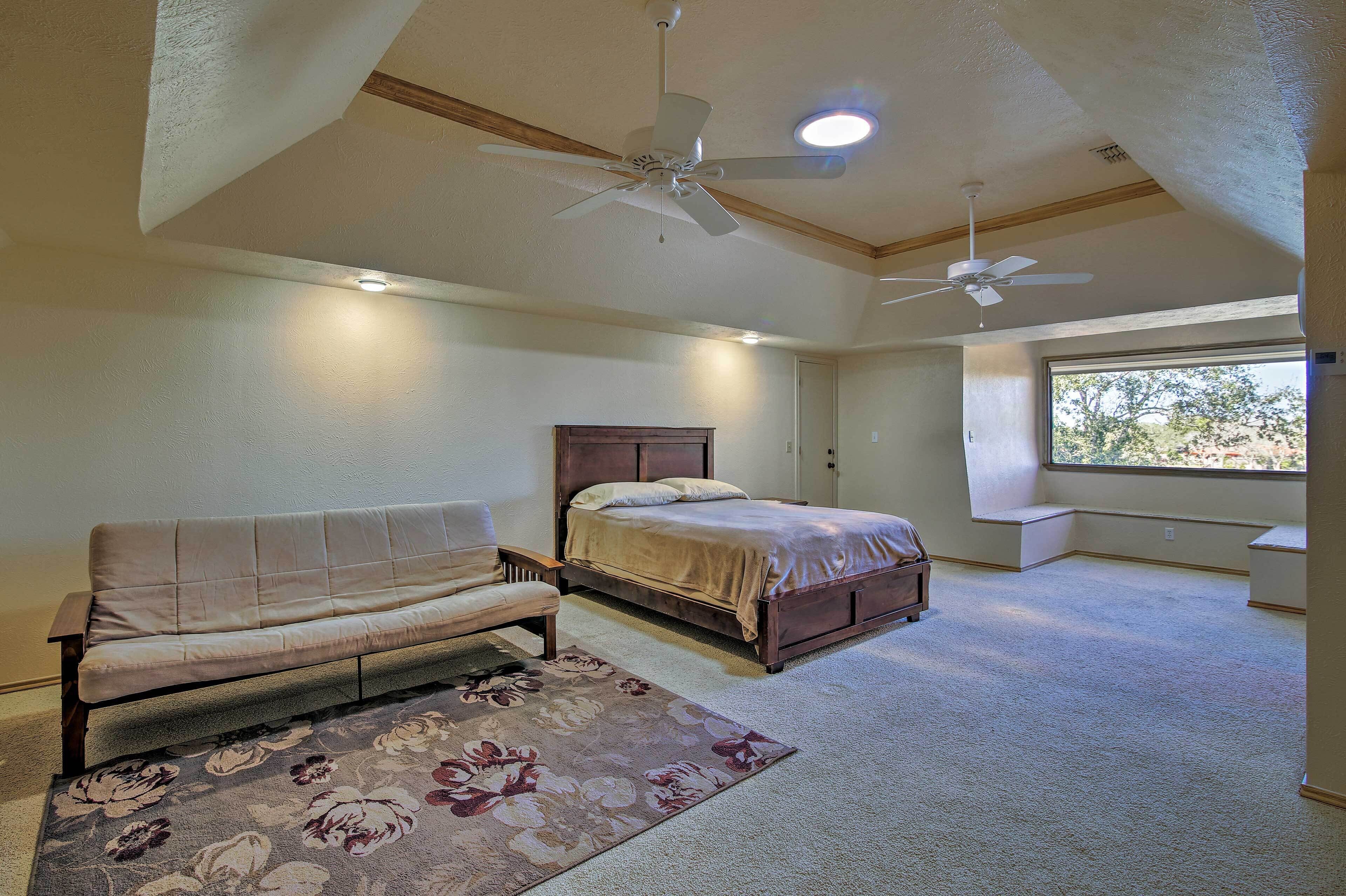A bedroom with a bed, a sofa, a ceiling fan, and a window.
