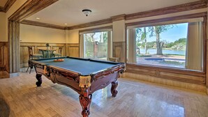 Una mesa de billar en una habitación con ventanas amplias, un comedor y vistas a un lago.