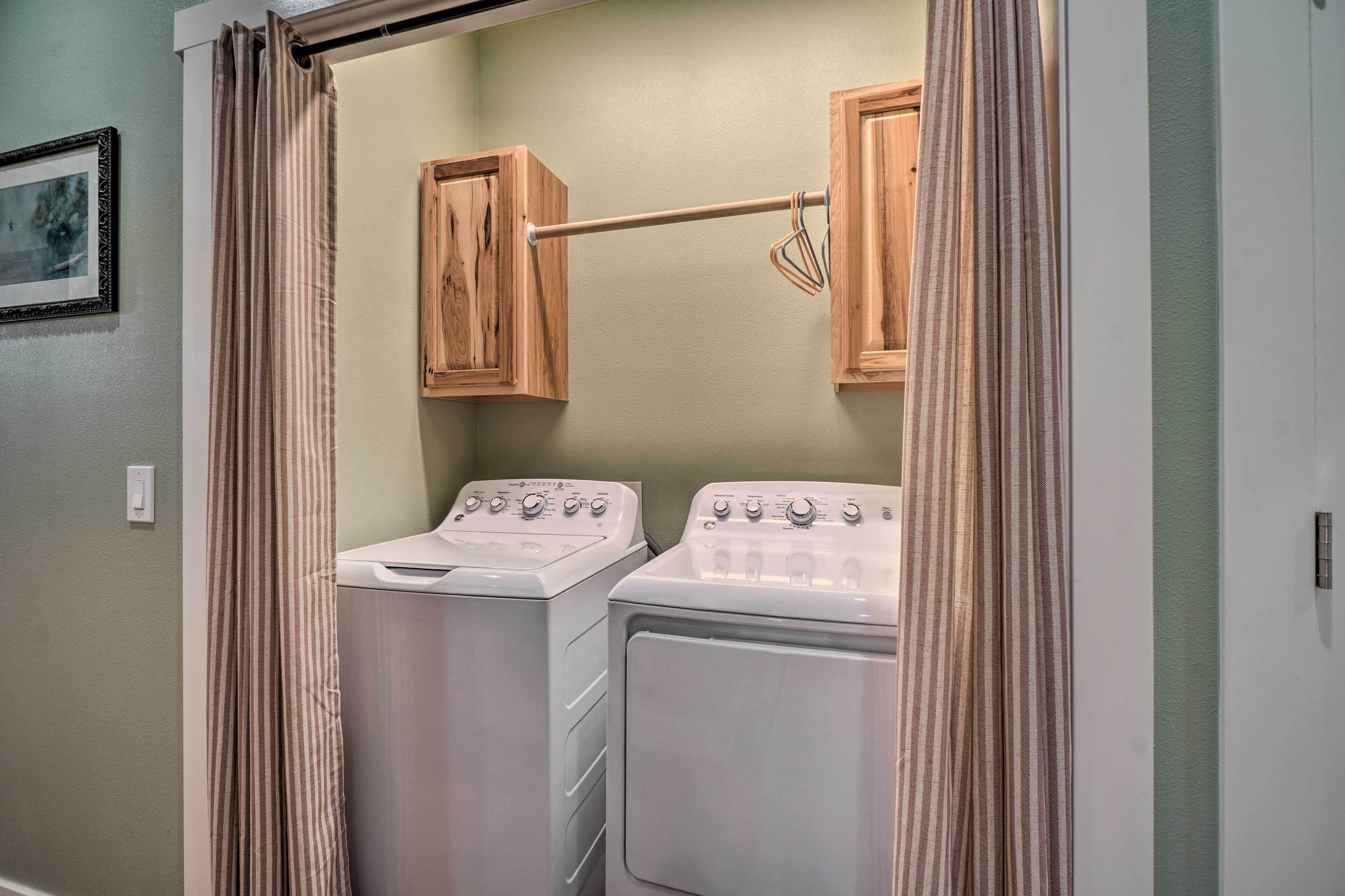 A laundry room with two stacked washer and dryer units, wooden cabinets above, and a metal drying rack.