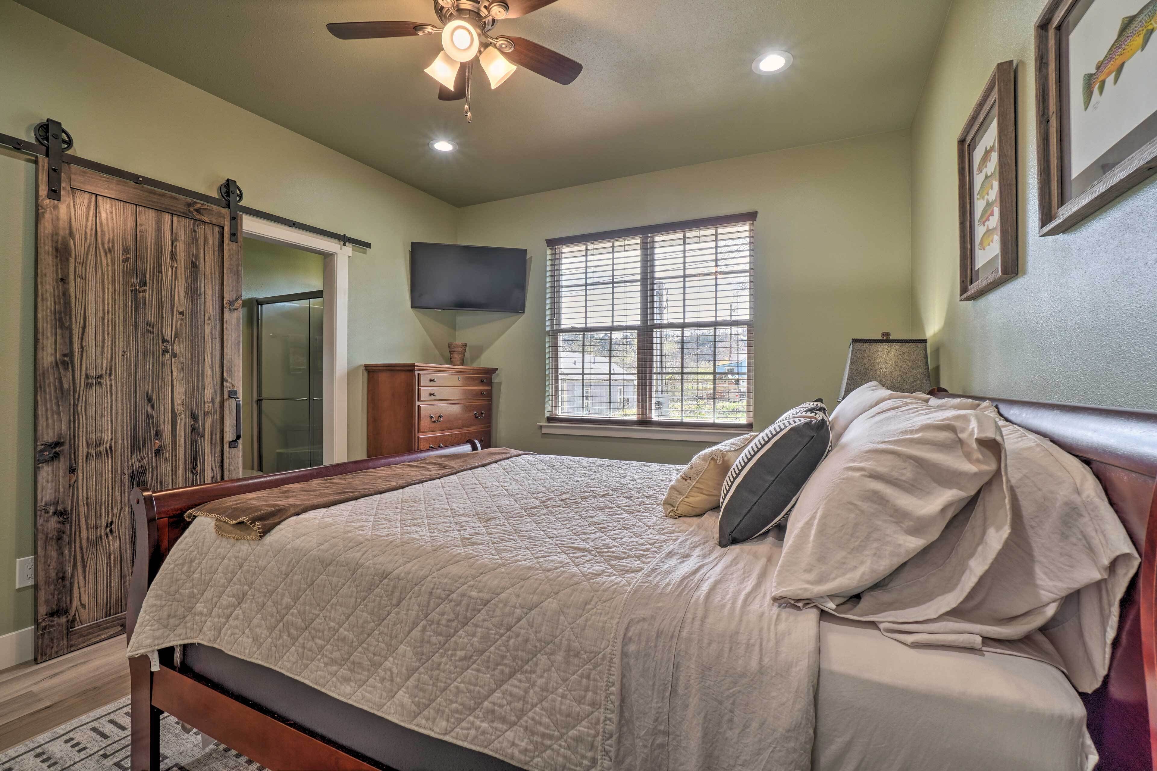 A bedroom with a bed, a ceiling fan, a window, and a TV mounted on the wall.