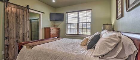 A bedroom with a bed, a ceiling fan, a window, and a TV mounted on the wall.