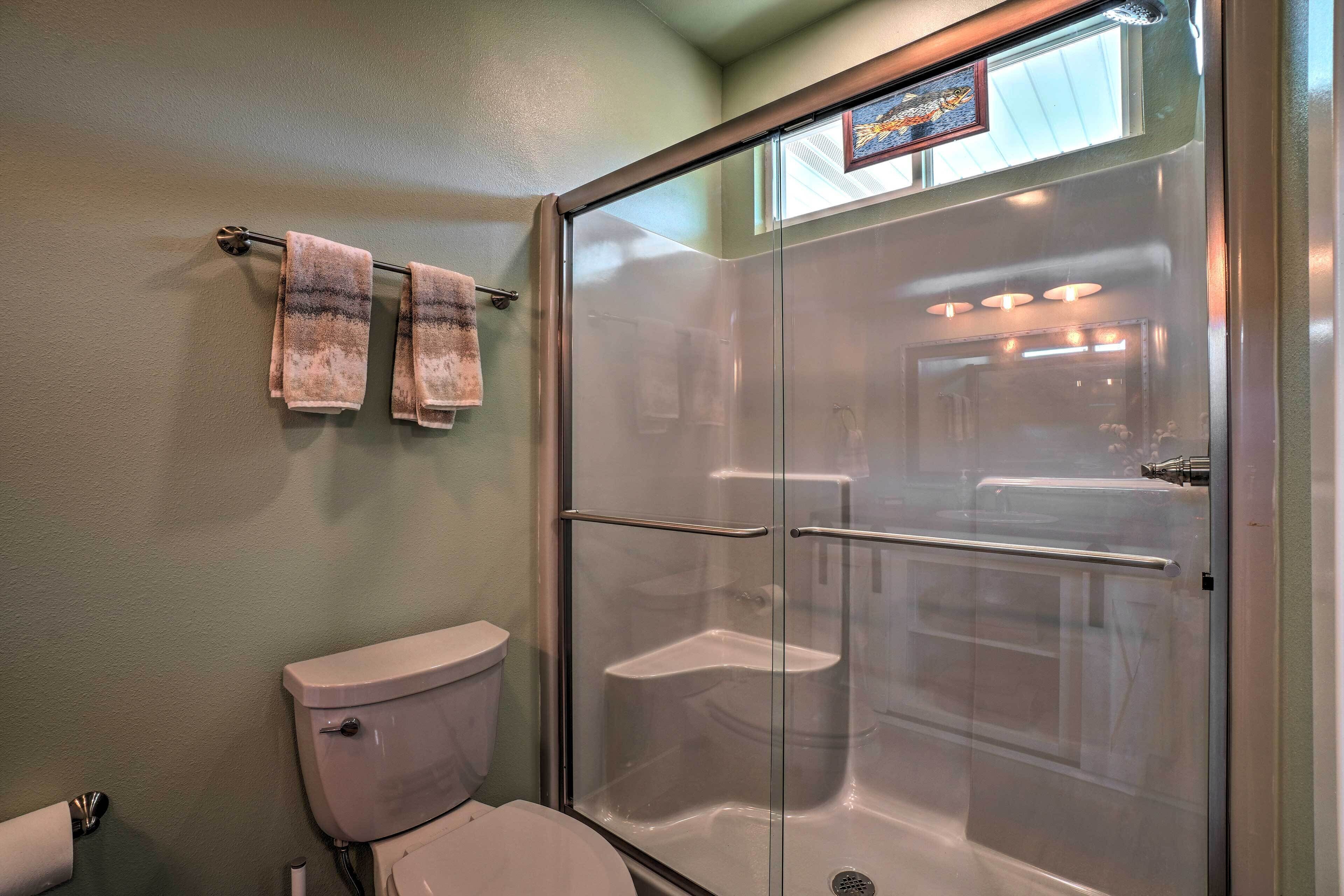 A bathroom with a glass-enclosed shower, a toilet, and a towel rack with two towels.