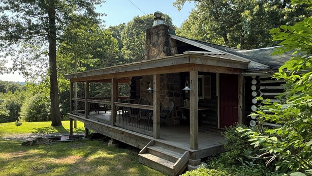A cabin with a covered porch, stone chimney, and a view of the surrounding forest. - Macungie Cabin w/ Fireplace Near Bear Creek Skiing (Macungie)