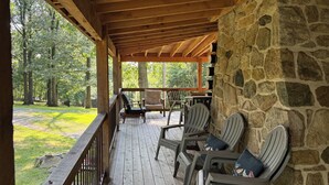 A covered outdoor deck with wooden flooring, stone walls, and several chairs with cushions. - Macungie Cabin w/ Fireplace Near Bear Creek Skiing (Macungie)