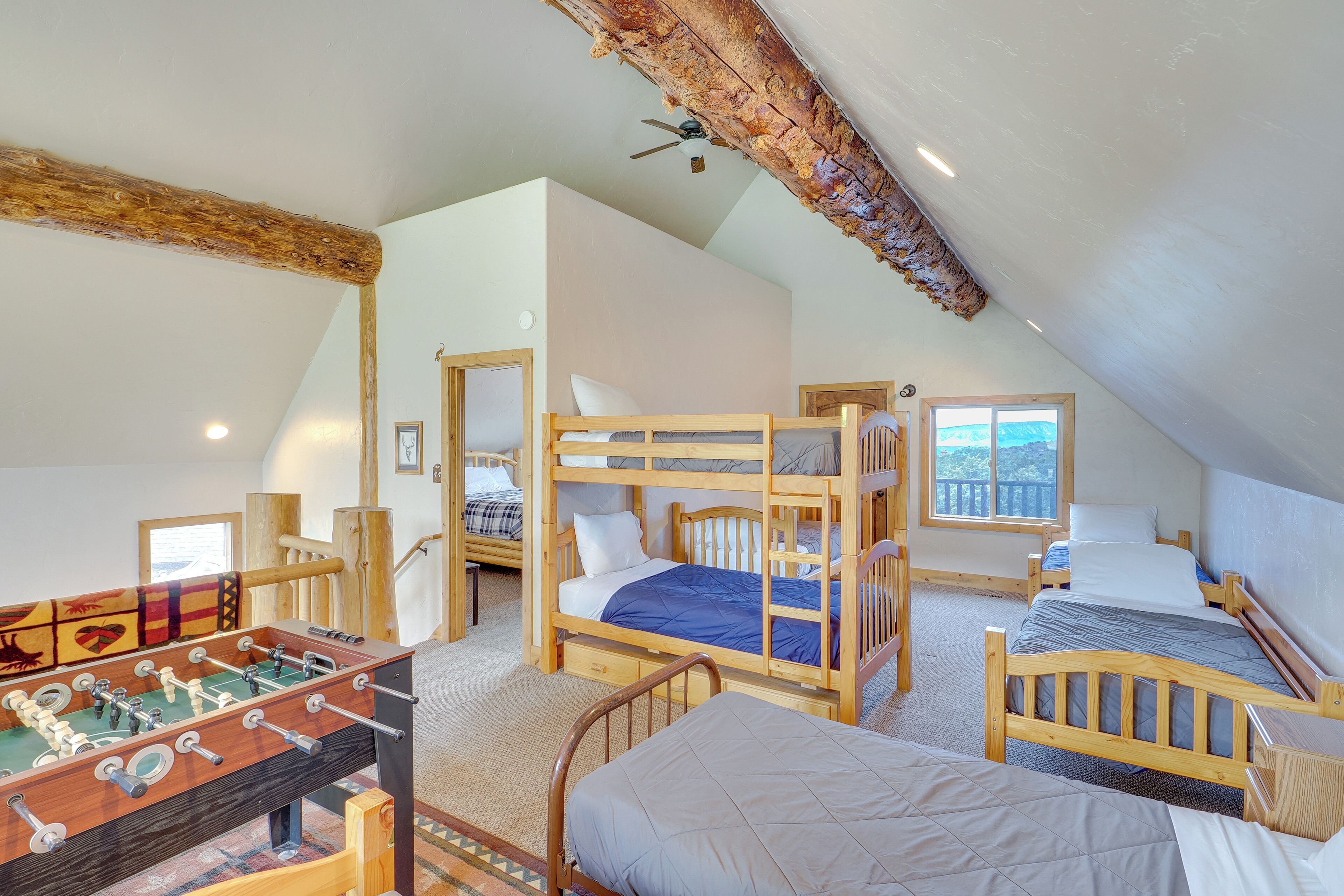 A dormitory-style room with bunk beds, a foosball table, and a window with a view.