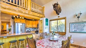 L’intérieur d’un chalet rustique comprend un coin repas, des tabourets de bar en bois, une tête de buffle montée au mur et une décoration murale sur le thème de la famille.